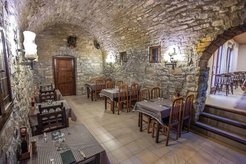 Comedor bajo bóvedas de piedra con mesas vestidas de blanco y luz cálida
